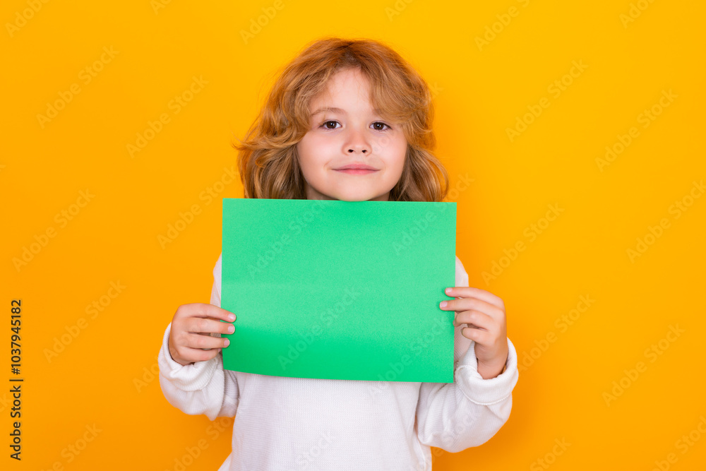 Child showing empty sheet of paper, isolated on yellow background. Portrait of a kid holding a blank placard, poster. Child showing empty sheet of paper, isolated on yellow background. Portrait of a kid holding a blank placard, poster.