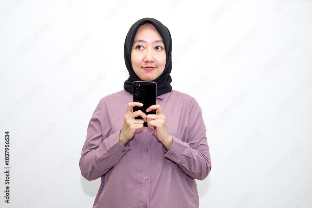 Portrait of Asian, Indonesian woman wearing shirt, hijab and holding mobile phone who is overwhelmed with emotions and bad thoughts, unhappy and stressed. Isolated on white background Portrait of Asian, Indonesian woman wearing shirt, hijab and holding mobile phone who is overwhelmed with emotions and bad thoughts, unhappy and stressed. Isolated on white background