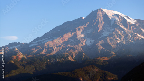 Mount Rainier during sunrise, aerial view with light cloud cover over forested mountains in Washington State, USA