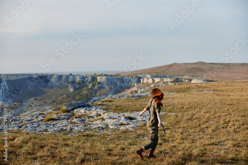 Woman in hat enjoying a serene mountain view while walking through a grassy field in nature