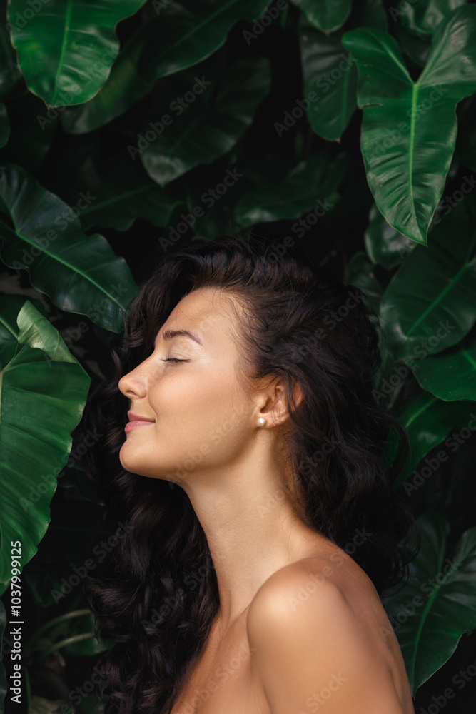A serene woman with curly hair and glowing skin poses with her eyes closed, enjoying a peaceful moment amidst lush tropical leaves. Perfect for wellness, beauty, and skincare campaigns that emphasize A serene woman with curly hair and glowing skin poses with her eyes closed, enjoying a peaceful moment amidst lush tropical leaves. Perfect for wellness, beauty, and skincare campaigns that emphasize
