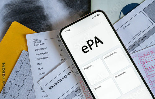 Ein Smartphone auf dem gerade eine elektronische Patientenakte angezeigt wird, liegt auf medizinischen Dokumenten, horizontal