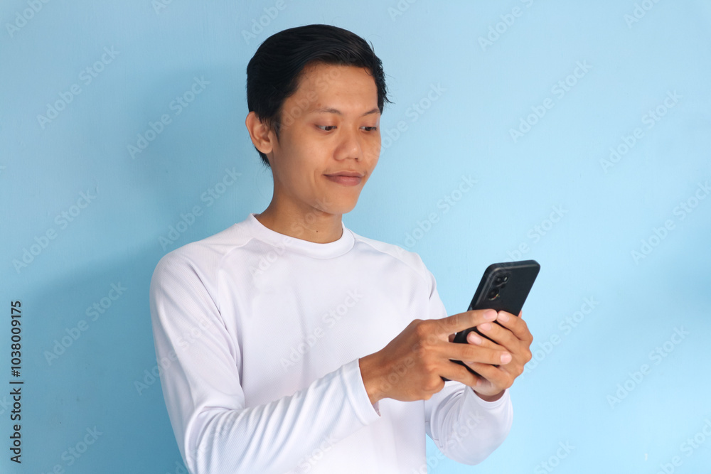 Young Asian man looking his mobile phone with happy expression Young Asian man looking his mobile phone with happy expression