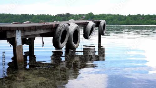 A dock with four tires on it is floating in a body of water. The tires are old and worn, and the dock itself is made of wood. The water is calm and still, with no visible waves or ripples
