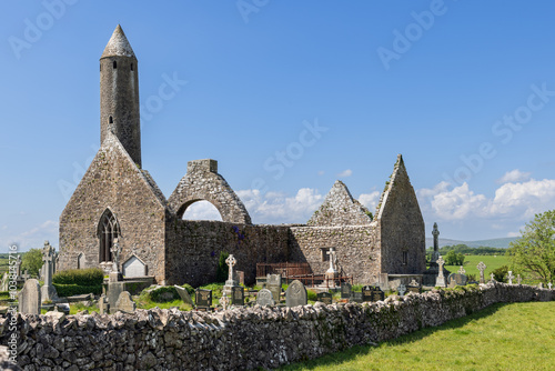 Kilmacduagh Abbey in County Galway, Ireland, features a round tower and medieval stone ruins surrounded by a historic cemetery