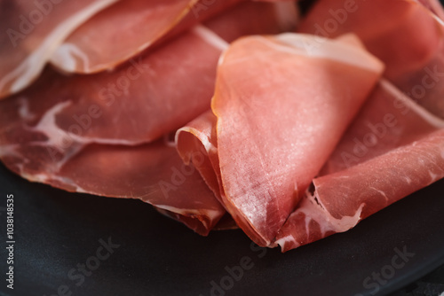 Thin italian prosciutto slices on black plate on conctere background closeup photo