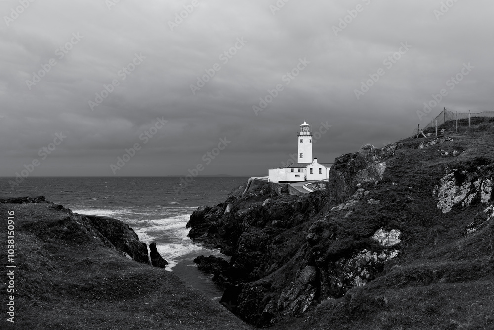 A monochrome photograph of Fanad Head Lighthouse during a storm, highlighting the sharp contrasts and textures of the sea, rocky cliffs, and dark clouds against the white of the lighthouse A monochrome photograph of Fanad Head Lighthouse during a storm, highlighting the sharp contrasts and textures of the sea, rocky cliffs, and dark clouds against the white of the lighthouse