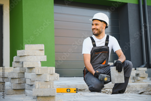 The master in gloves lays paving stones in layers. Garden brick pathway paving by professional paver worker. Laying gray concrete paving slabs in house courtyard on sand foundation base