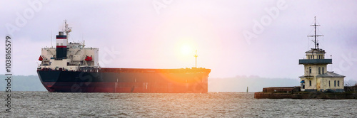 A cargo ship navigates through coastal waters near a lighthouse under a twilight sky photo