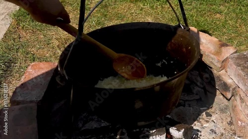 A traditional Romanian cooking scene showing onions being sautéed in a cauldron over a wood fire, a key step in making authentic zacusca. The rustic outdoor setup highlights the time-honored methods. photo