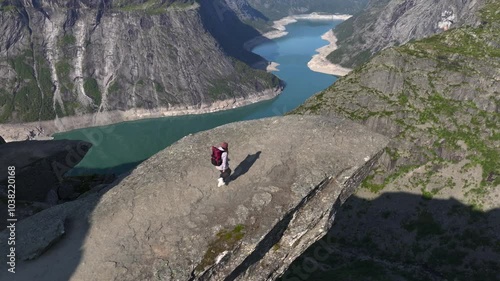 Girl with Backpack on the edge of cliff on Trolltunga, Norway. Aerial of Norwegiant Highlight SIghtseeing Troll Tongue
