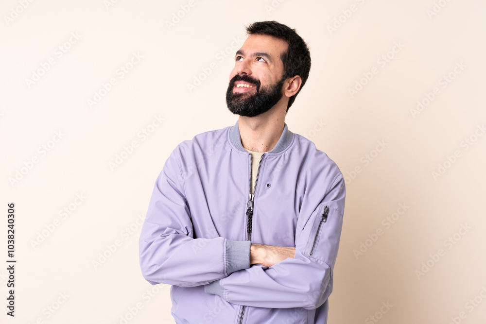 Caucasian man with beard wearing a jacket over isolated background looking up while smiling Caucasian man with beard wearing a jacket over isolated background looking up while smiling