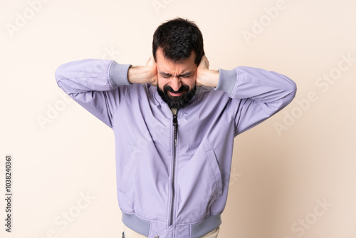 Caucasian man with beard wearing a jacket over isolated background frustrated and covering ears