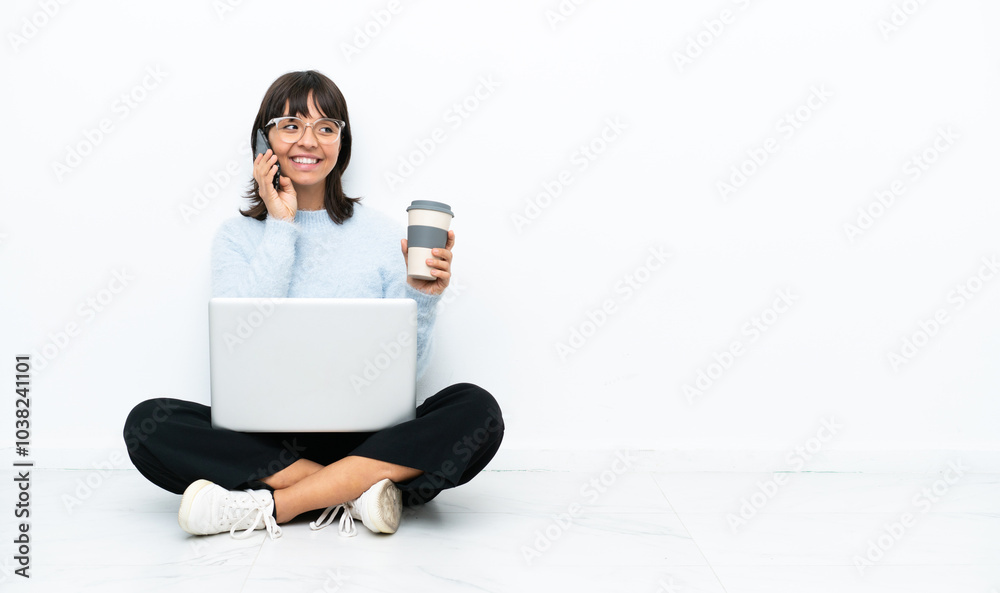 Young mixed race woman sitting on the floor with laptop isolated on white background holding coffee to take away and a mobile Young mixed race woman sitting on the floor with laptop isolated on white background holding coffee to take away and a mobile