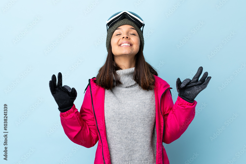 Mixed race skier girl with snowboarding glasses over isolated blue background in zen pose. Mixed race skier girl with snowboarding glasses over isolated blue background in zen pose.