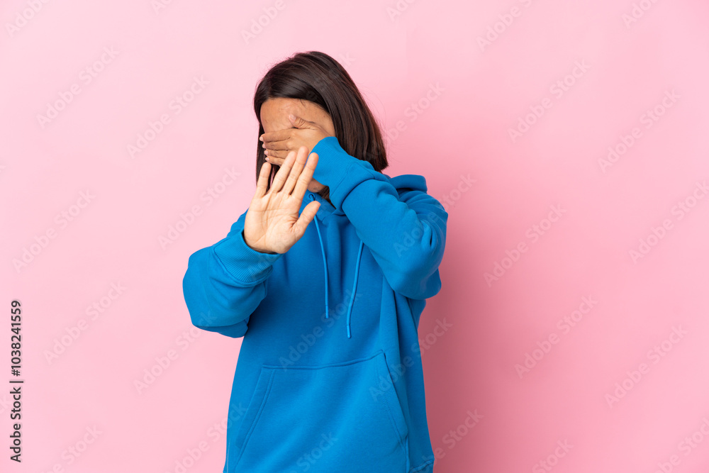 Young latin woman isolated on pink background making stop gesture and covering face Young latin woman isolated on pink background making stop gesture and covering face