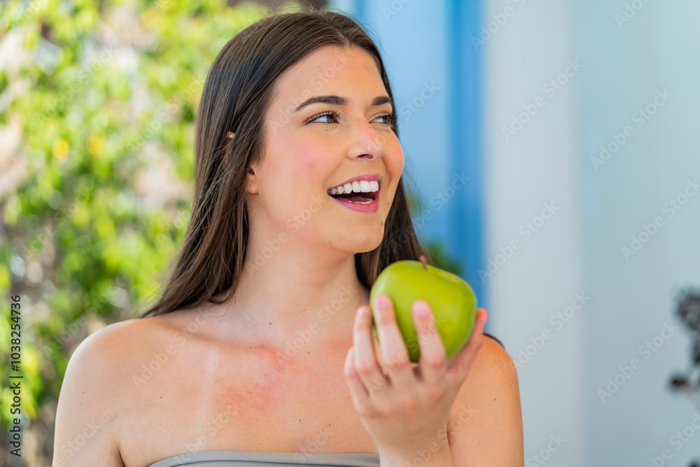 Young pretty Brazilian woman at outdoors holding an apple with happy expression Young pretty Brazilian woman at outdoors holding an apple with happy expression