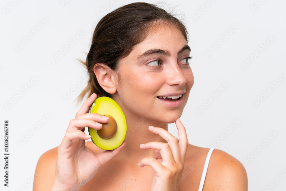 Young Pretty caucasian woman isolated on white background holding an avocado while smiling. Close up portrait