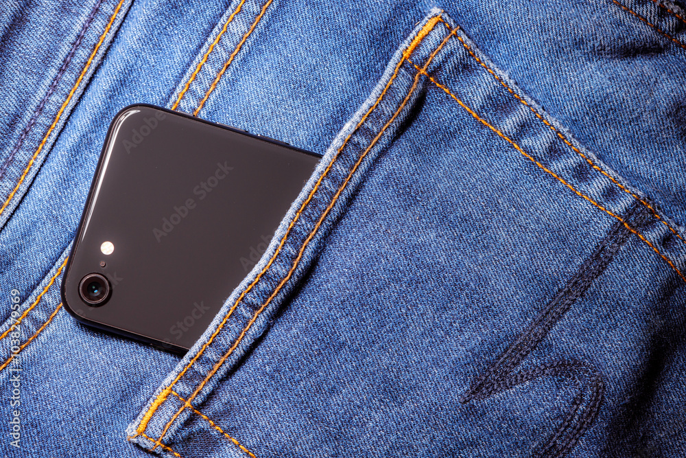 Worn denim trousers. Machine stitch close up. Denim texture in blue. The concept of repairing old clothes. Sewing factory. A smartphone is peeking out of the pocket of his jeans. Worn denim trousers. Machine stitch close up. Denim texture in blue. The concept of repairing old clothes. Sewing factory. A smartphone is peeking out of the pocket of his jeans.