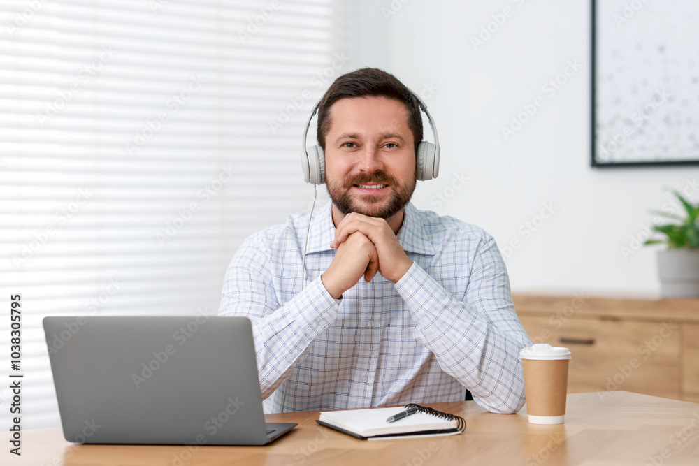 Interpreter in headphones having video chat via laptop at wooden table indoors Interpreter in headphones having video chat via laptop at wooden table indoors