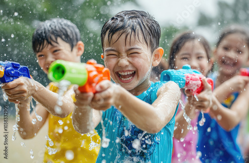 Asian children having fun playing with water guns in the park, a summer outdoor background.
