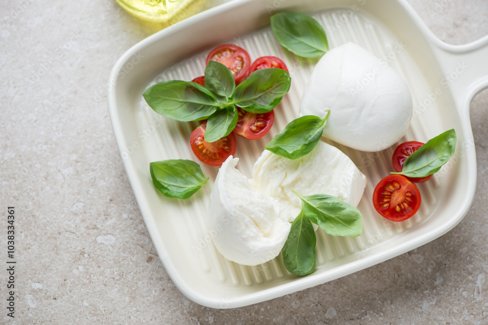 Serving tray with buffalo mozzarella, cherry tomatoes and basil, horizontal shot on a beige stone surface, elevated view Serving tray with buffalo mozzarella, cherry tomatoes and basil, horizontal shot on a beige stone surface, elevated view
