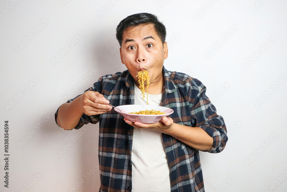 Young handsome trendy asian man eating yummy hot and spicy instant noodle using fork isolated on white background. Asian guy servile end of the month with cheap food. Young handsome trendy asian man eating yummy hot and spicy instant noodle using fork isolated on white background. Asian guy servile end of the month with cheap food.