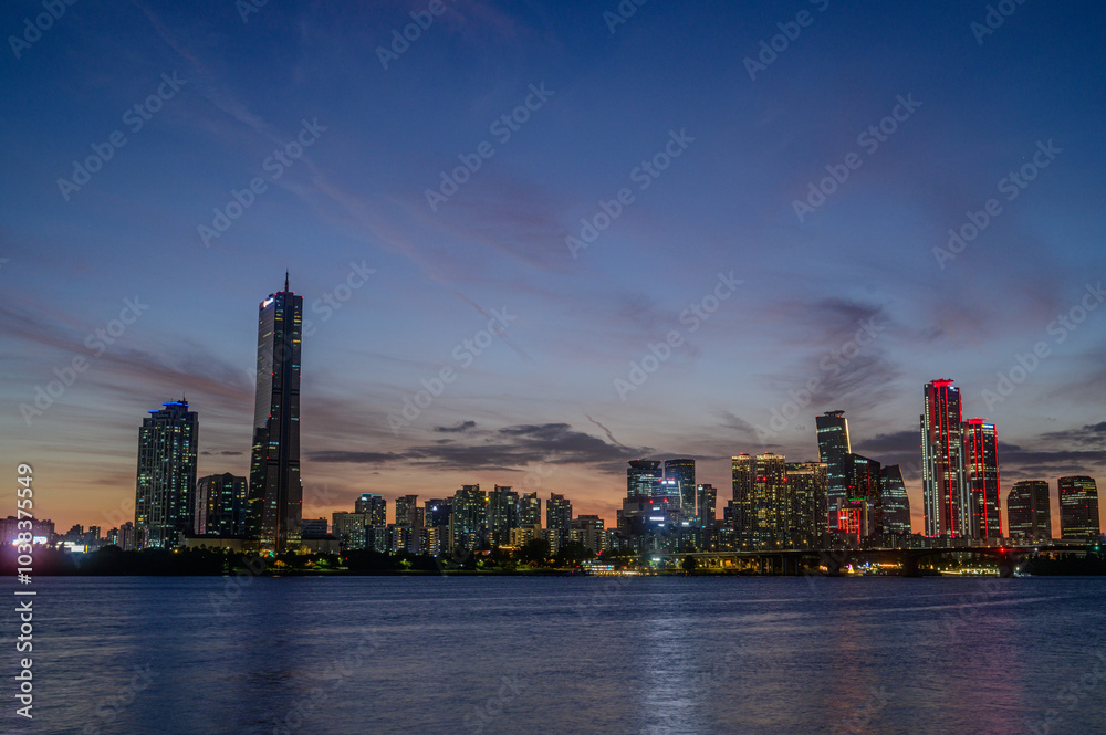 Obraz premium Sunset and silhouette view of 63 Building and high rise buildings of financial district with Wonhyo Bridge on Han River at Yeouido near Yeongdeungpo-gu, Seoul, South Korea