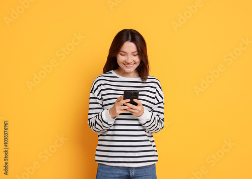 Smiling young woman using smartphone on yellow background