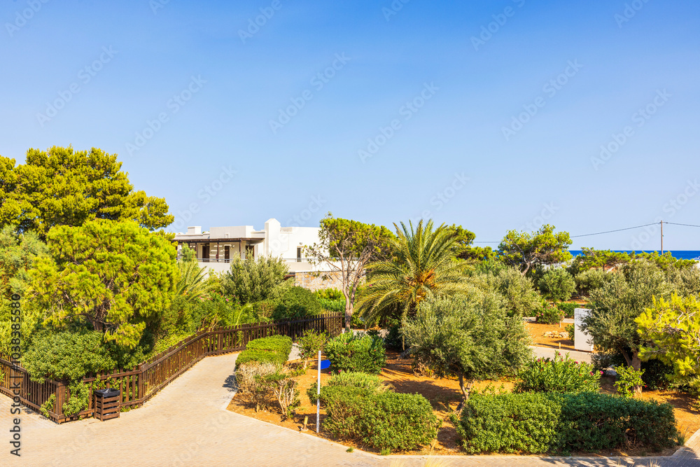 Green garden with trees and bushes, building in background, and clear blue sky in peaceful resort setting. Crete. Greece. Green garden with trees and bushes, building in background, and clear blue sky in peaceful resort setting. Crete. Greece.