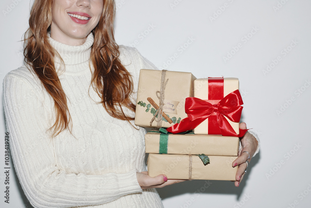 Woman smiling while holding wrapped Christmas gifts with red and green ribbons and bow in a well-lit environment Woman smiling while holding wrapped Christmas gifts with red and green ribbons and bow in a well-lit environment