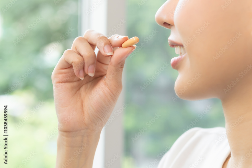 Dietary supplement, asian young woman, girl hand holding orange medical pill, take or eat vitamin C, D for treatment for skin, hair and nail strengthen near window in living room at home, healthcare. Dietary supplement, asian young woman, girl hand holding orange medical pill, take or eat vitamin C, D for treatment for skin, hair and nail strengthen near window in living room at home, healthcare.