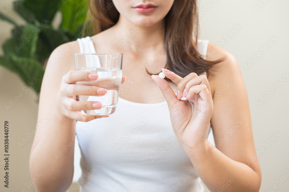 Sick asian young woman, girl holding tablet pill on hand, painkiller medicine from fever, stomach pain, headache for treatment, take drug or vitamin with glass of water at home. Health care concept. Sick asian young woman, girl holding tablet pill on hand, painkiller medicine from fever, stomach pain, headache for treatment, take drug or vitamin with glass of water at home. Health care concept.