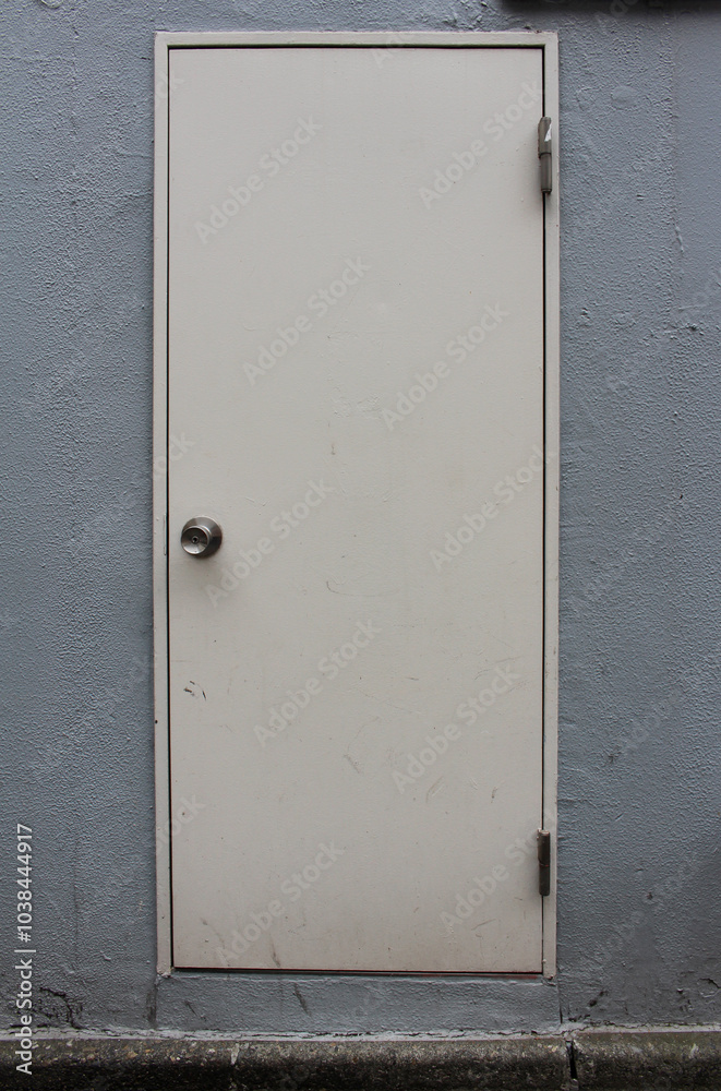 Back door of a building in a street. White door with metal doorknob on grey wall background. Back door of a building in a street. White door with metal doorknob on grey wall background.