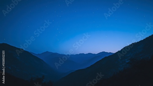 A mountain range under a deepening blue sky, where stars and the galaxy become visible in the growing darkness.