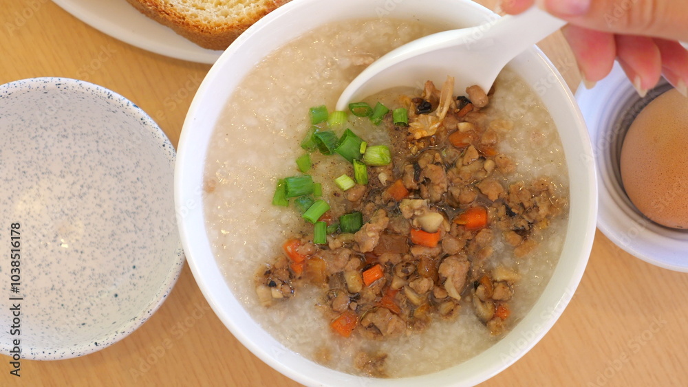 Close-up of congee with minced pork, green onions, carrots on wooden table. Comfort Food and Traditional Cuisine Close-up of congee with minced pork, green onions, carrots on wooden table. Comfort Food and Traditional Cuisine