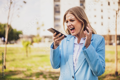 Image of angry businesswoman screaming on the phone while standing outdoor.	 photo