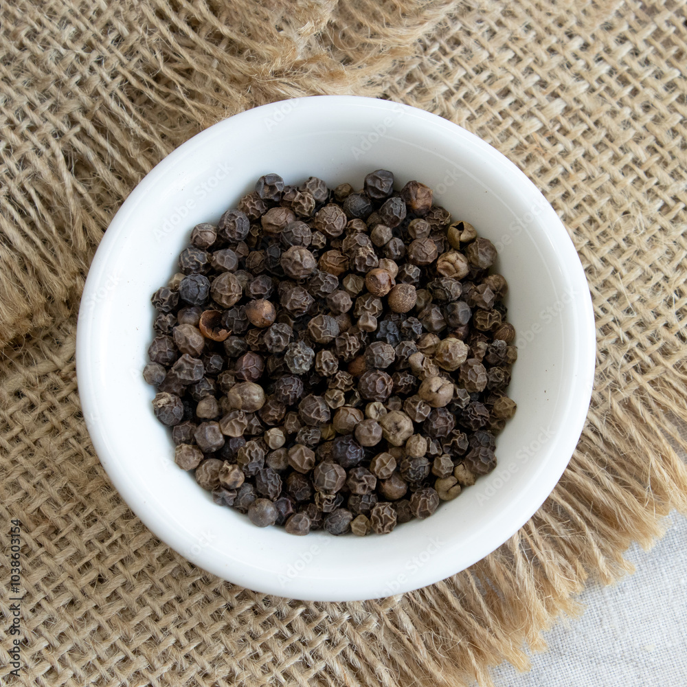 Pile of Black peppercorns Black pepper dried seeds in wooden spoon on linen background Pile of Black peppercorns Black pepper dried seeds in wooden spoon on linen background