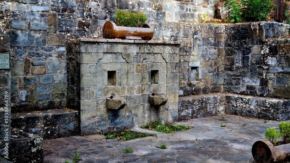 An old stone fountain with two basins sits against a stone wall