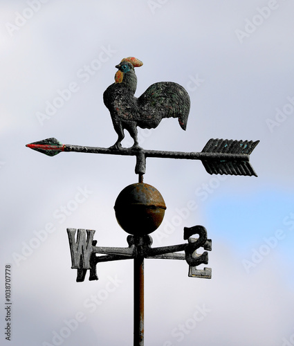 iron rooster weather vane sits atop the roof pointing to the wind direction with its arrow and cardinal letters photo