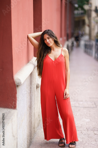 An Elegant Woman Dressed in a Stunning Red Jumpsuit Posing Gracefully Against a City Wall