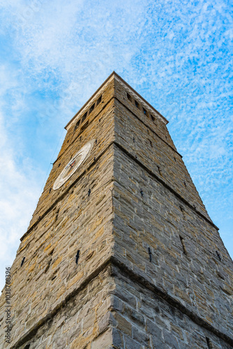 Steinerner Uhrturm, der sich majestätisch in den blauen Himmel erstreckt. Perspektive von unten Textur des Mauerwerks und Licht-Schatten-Spiel betonen Struktur und Tiefe. Weicher, blauer Himmel. photo