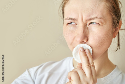 Woman contemplating skincare routine with cotton pad in natural light indoor setting for self-care and wellness concept. photo