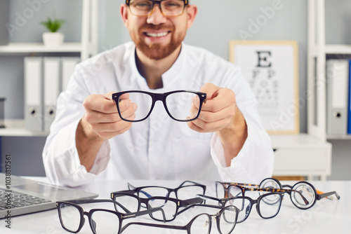 Ophthalmologist showing glasses, smiling doctor in clinic, helping to choose correct medical vision service. Solving optometry problems, eyes testing, prescribing contact lenses in optical store  photo