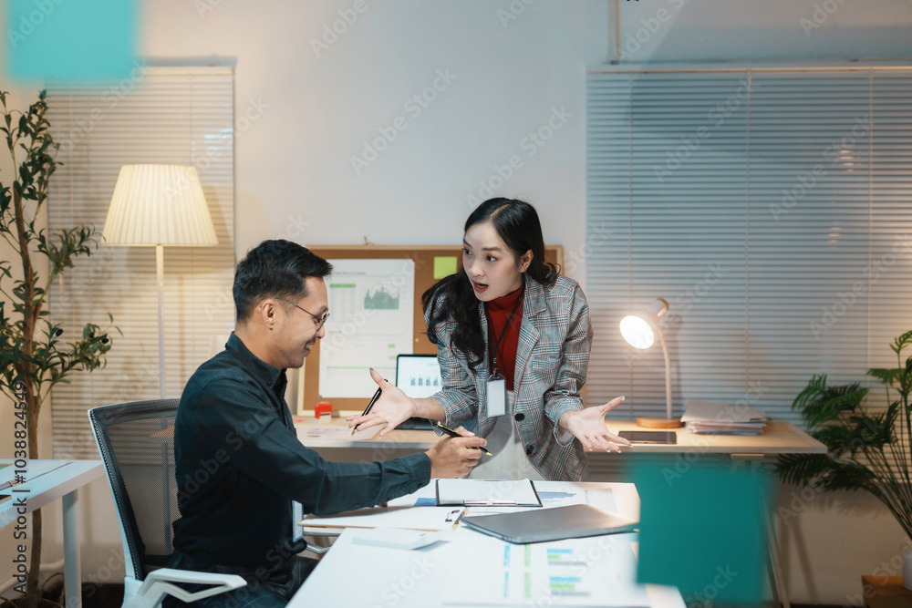 Obraz premium Businesswoman is standing and arguing with a businessman who is sitting at his desk in a brightly lit office working late into the night