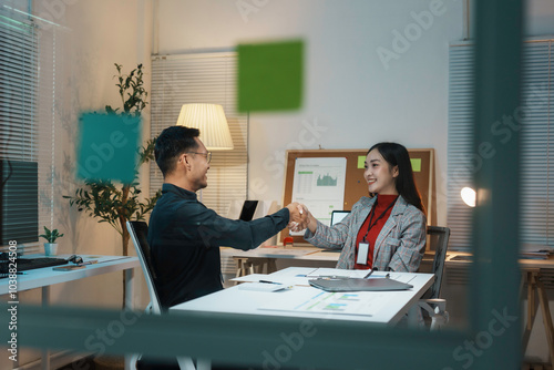 Two business people shaking hands in brightly lit office at night after closing a deal photo