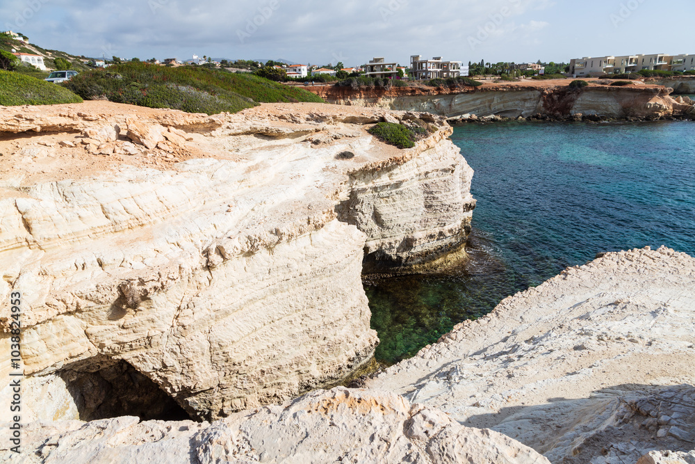 Peyia, Paphos, Cyprus - 8 November 2023: Secluded beach and limestone rock formations, Sea Caves and villas or a hotel in the background Peyia, Paphos, Cyprus - 8 November 2023: Secluded beach and limestone rock formations, Sea Caves and villas or a hotel in the background