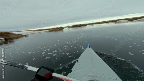 A kayaker floats down a cold river in the Arctic, surrounded by ice floes and a stunning gray sky
