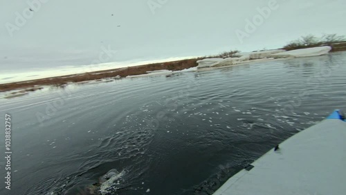 A kayaker paddles through a river with melting ice, navigating through floating chunks of ice in the spring