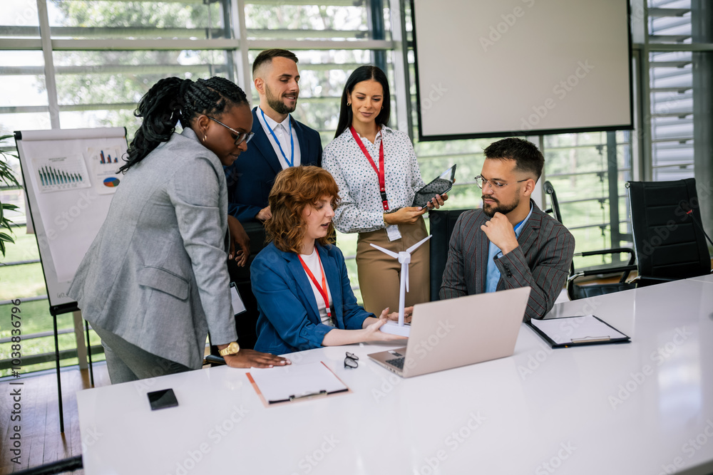 Multiracial business people talking about sustainable energy. They have windmill on a table and they are doing something on a laptop. Multiracial business people talking about sustainable energy. They have windmill on a table and they are doing something on a laptop.